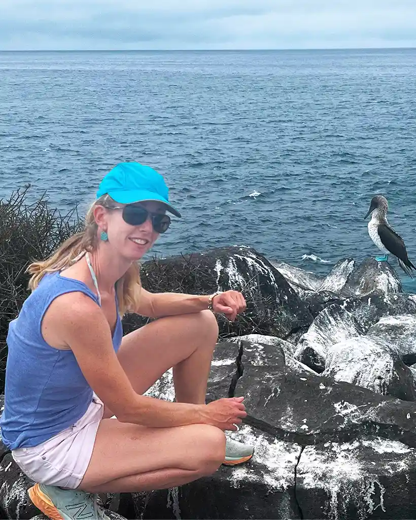 Carolina exploring the Galápagos with a blue-footed booby nearby Carolina sitting on coastal rocks next to a blue-footed booby in the Galápagos
