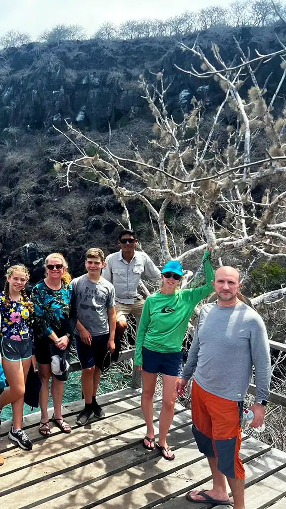 Carolina exploring the Galápagos with her retreat group Carolina standing with a retreat group on a wooden platform by rocky cliffs in the Galápagos Islands