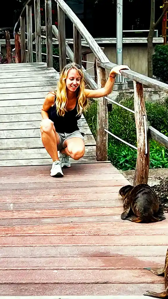 Carolina kneeling on a wooden walkway while observing a Galápagos sea lion Carolina connecting with a sea lion in the Galápagos Islands